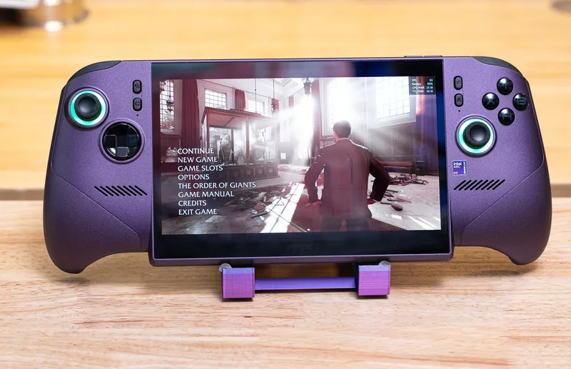 A purple handheld with lit-up joysticks and the intensive Indiana Jones game on screen, facing the camera, on a purple 3D-printed stand.