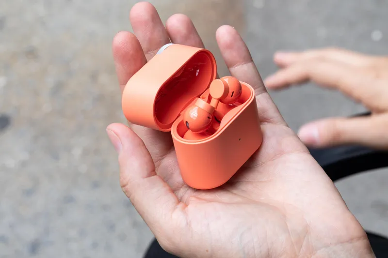 A hand holding the coral-colored CMF Clip Pro earbuds in their flip-top case.
