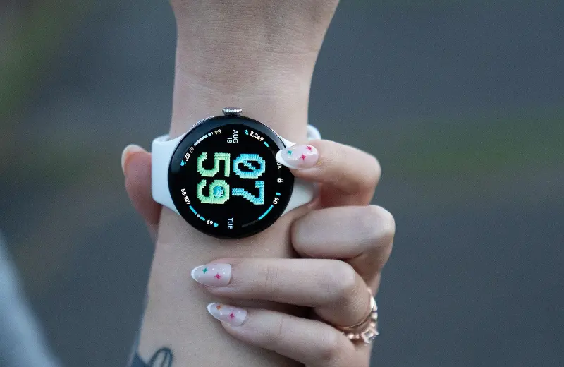 Close up of the Pixel Watch 5 with an AI generated watch face depicting cross-stitch texture on a retro font with some cute and fat woodland creatures in the numbers in a blue and green theme.