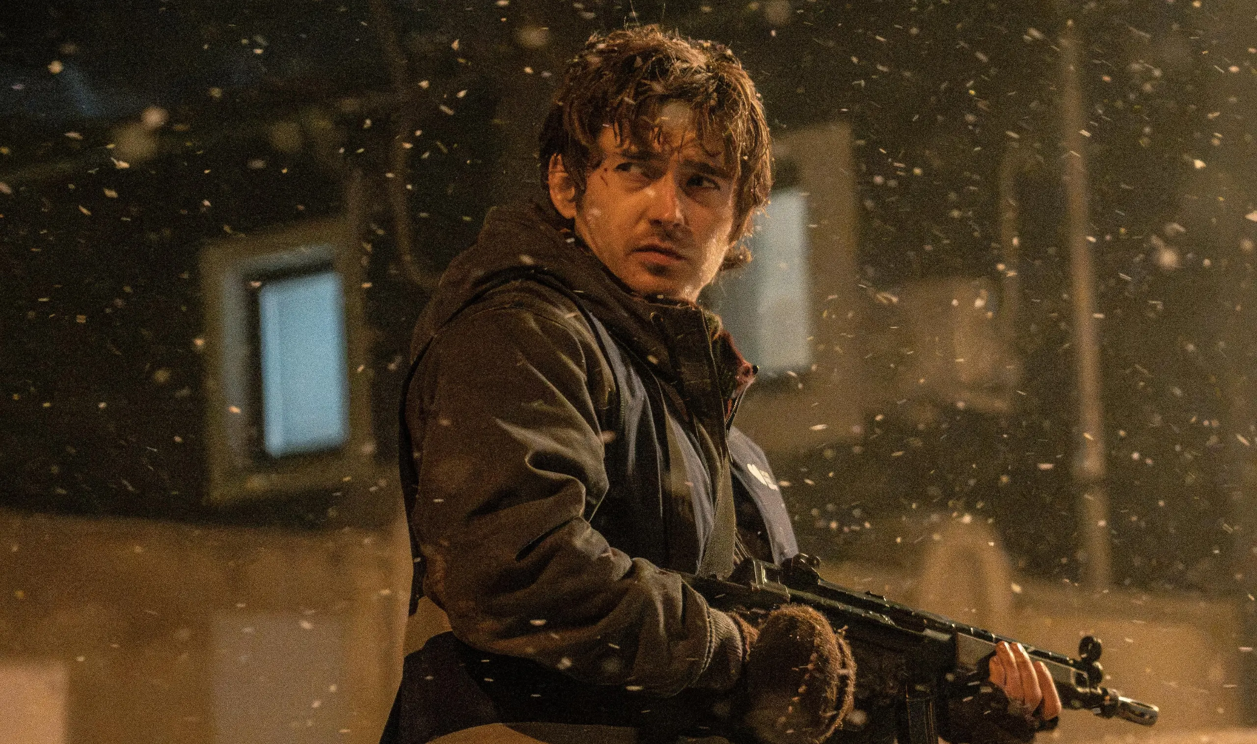A man in winter clothing standing in the middle of a city street while holding a gun.