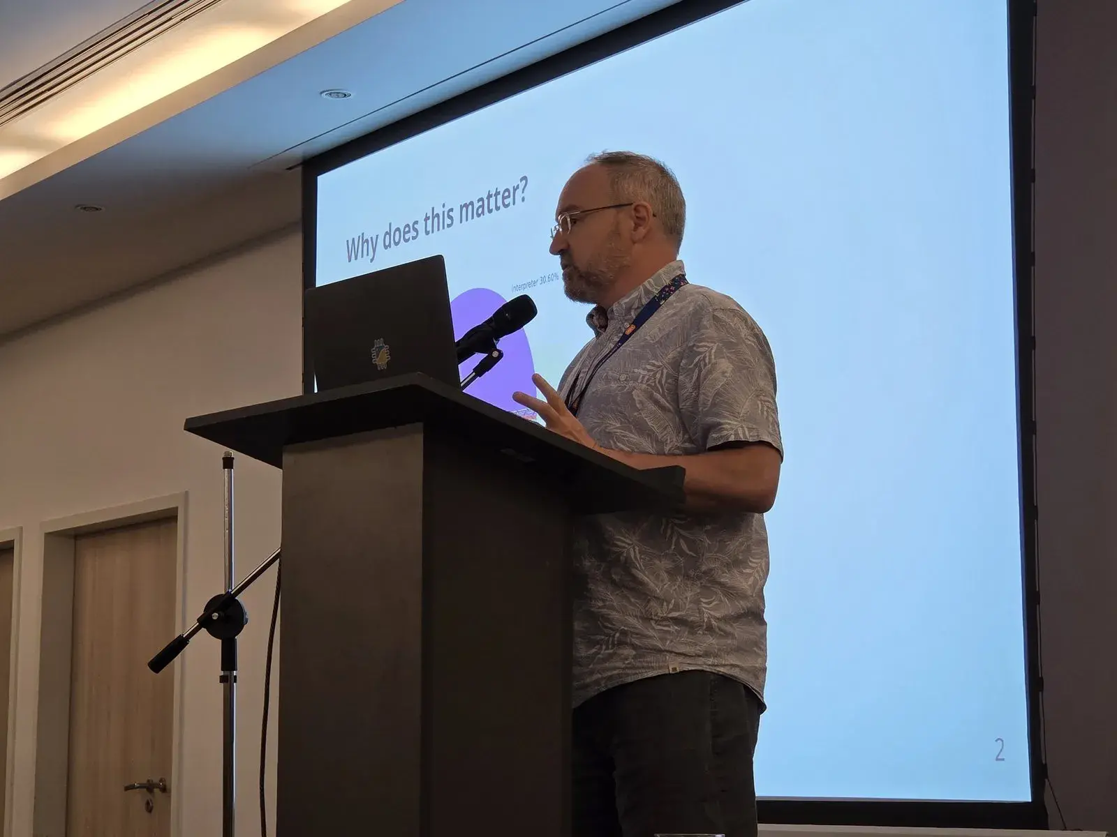 Mark Shannon speaking at the lectern, in front of a slide asking “Why does this matter?”