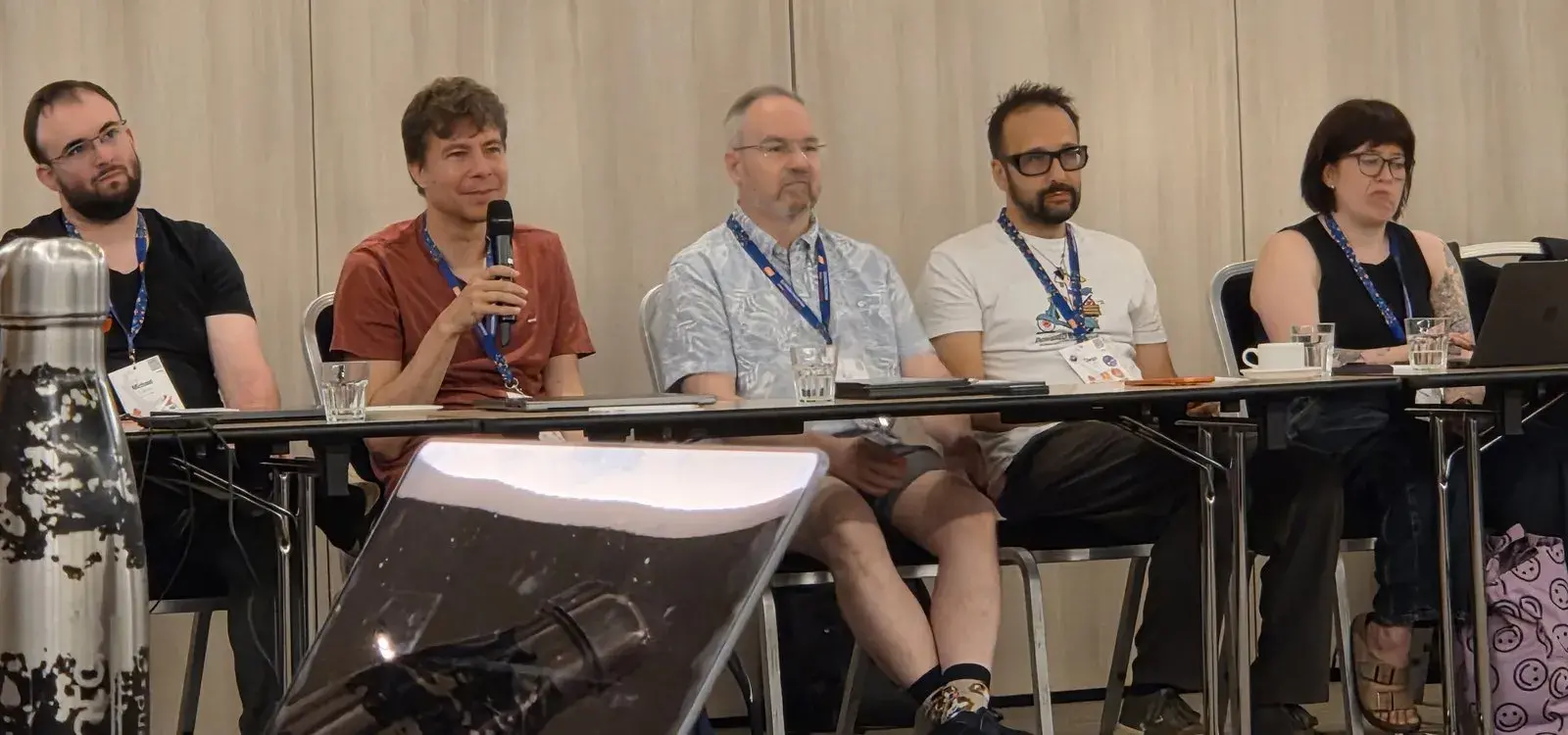 Jukka Lehtosalo speaking into a microphone, seated in a row of attendees