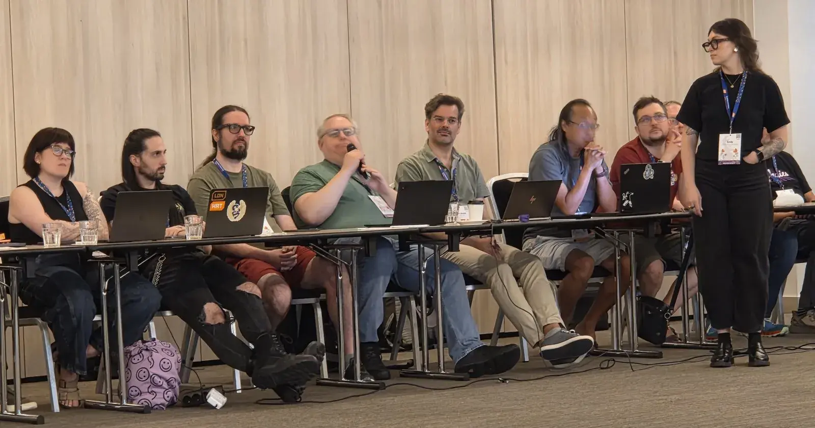 Larry Hastings speaking into a microphone, seated in a row of attendees