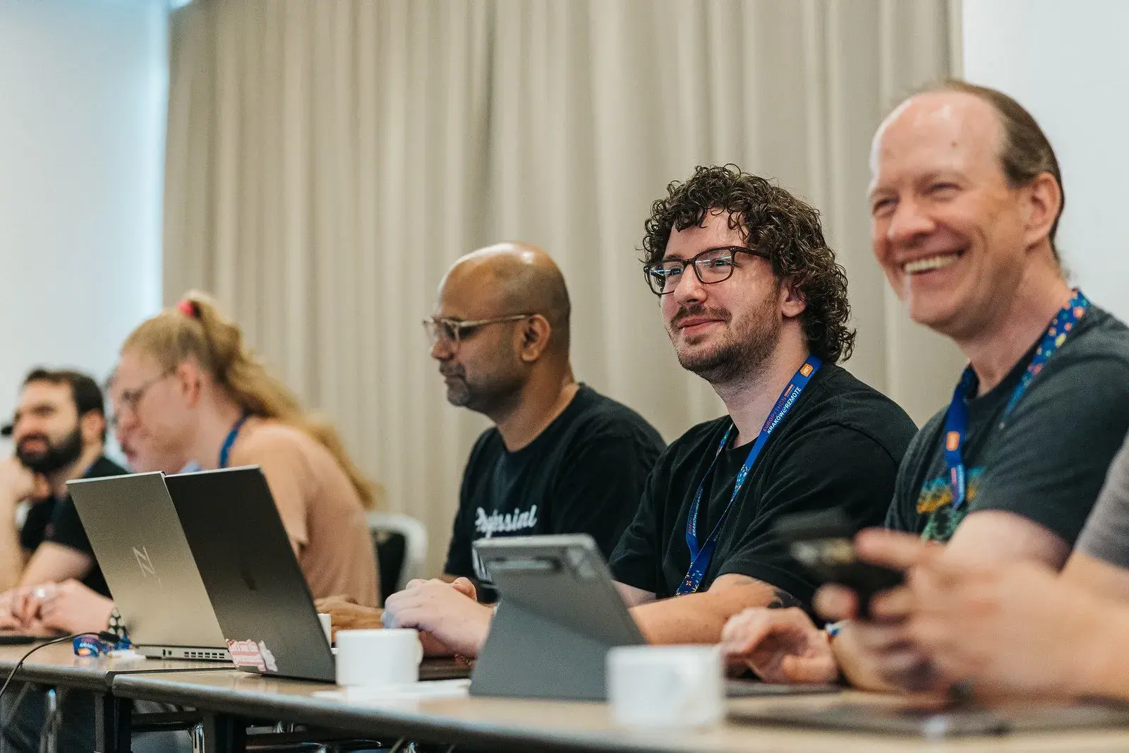 A row of smiling attendees seated at the table with their laptops