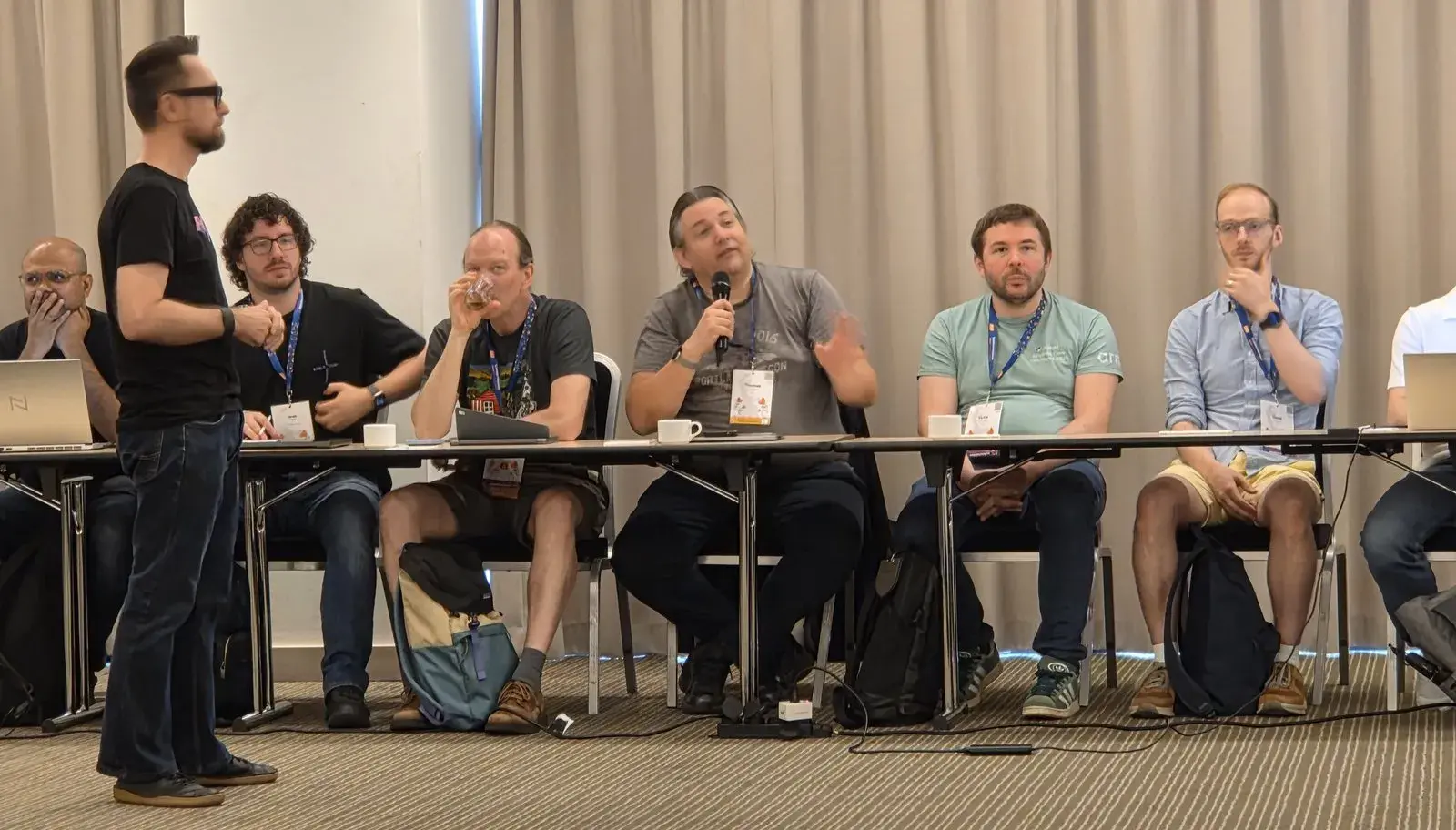 Thomas Wouters speaking into a microphone from his seat at the table, with other attendees beside him