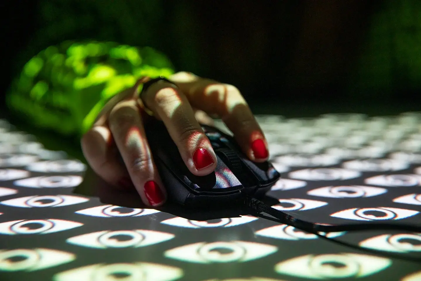 Photograph of a hand wearing red nail varnish holding a mouse with a projection overlay of stylized eyes