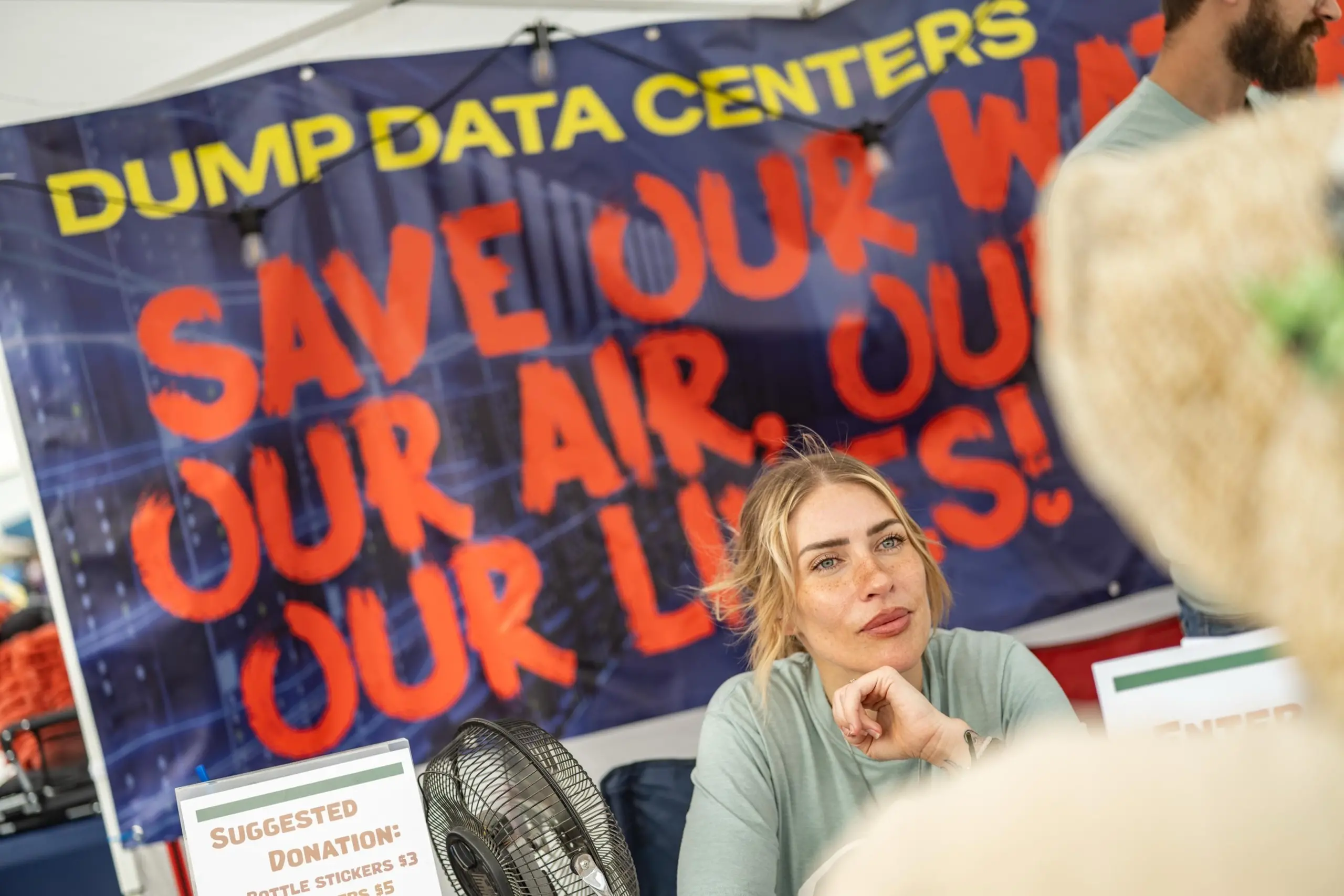 A woman tabling against data centers in front of a large vinyl sign that reads "dump data centers."