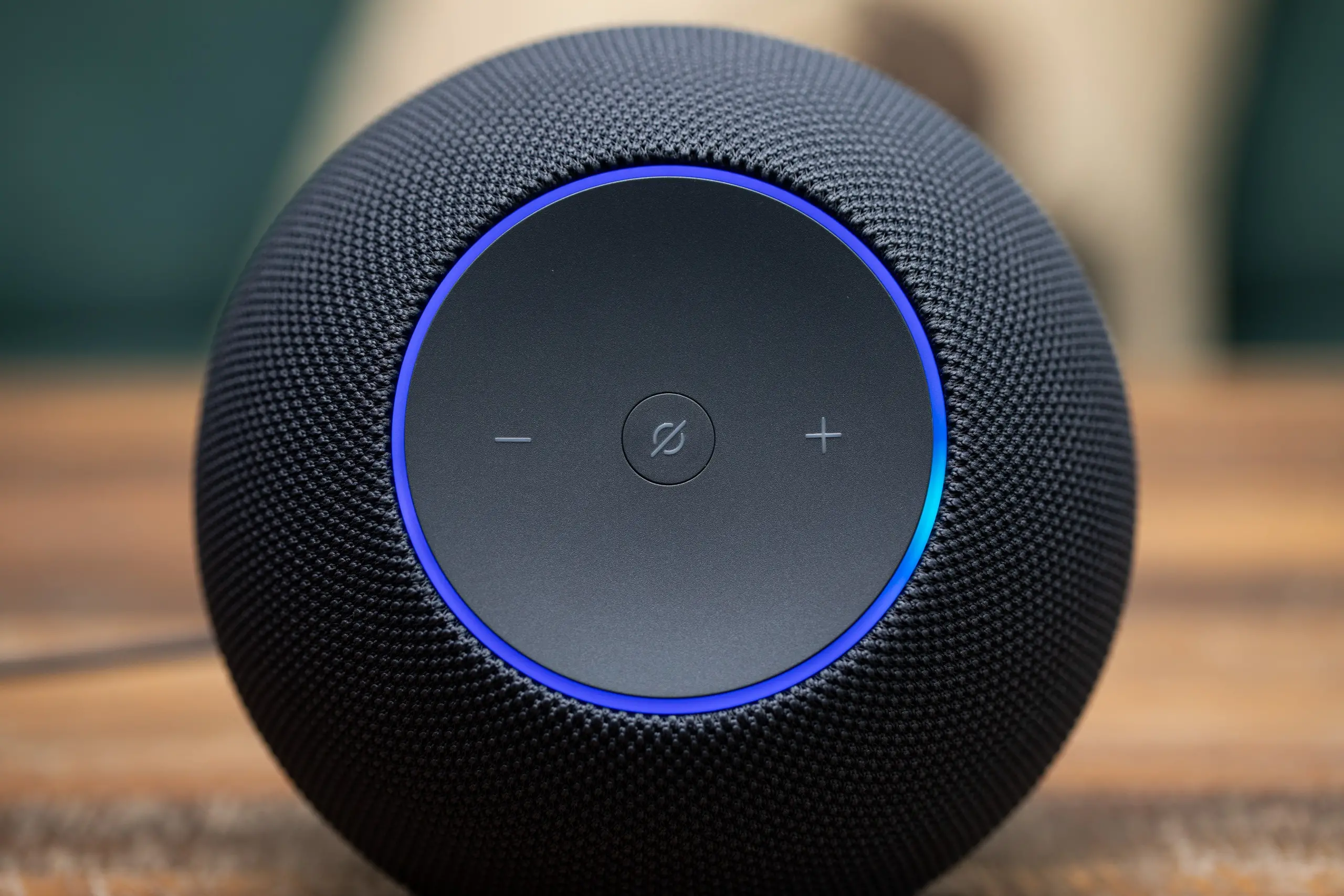 The Amazon Echo Studio with its front blue LED ring illuminated while sitting on a wooden coffee table.