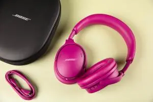 Gen 2 Bose QuietComfort Headphones sitting on a pale yellow surface next to a USB-C charger and black Bose case.
