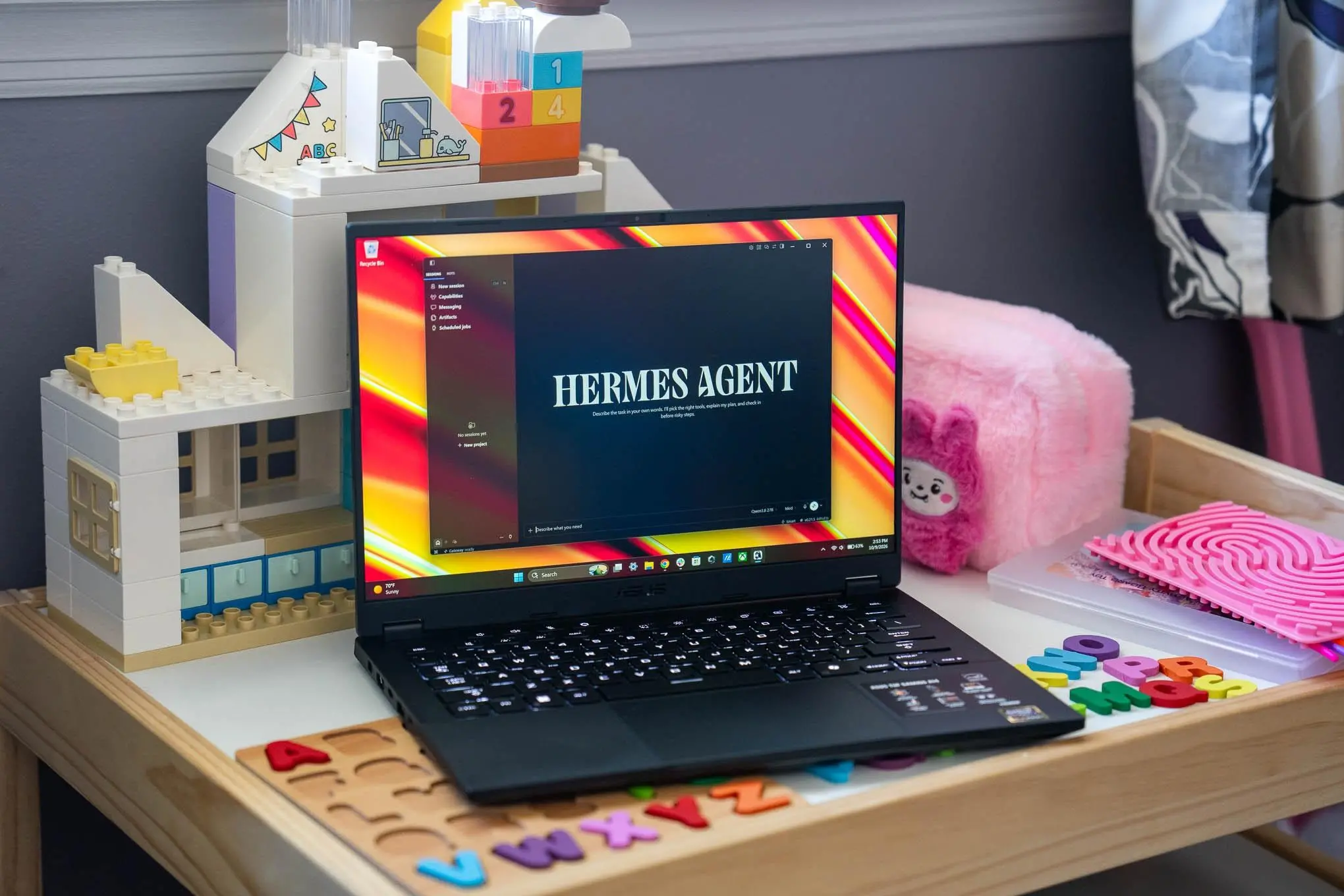 An Asus TUF A14 laptop running Hermes Agent local AI and sitting on a child’s table full of toys.