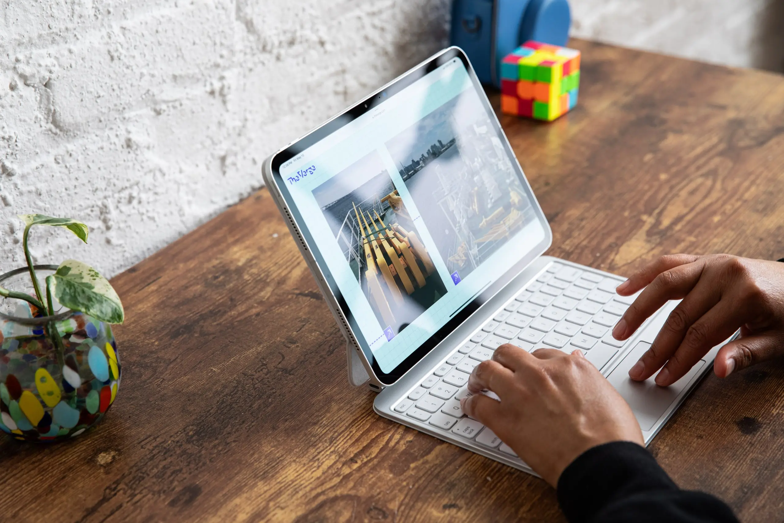 A photo of someone using an iPad Pro M4 with its Magic Keyboard. It looks a lot like a laptop! The iPad and keyboard are on a wooden table with a white brick background.