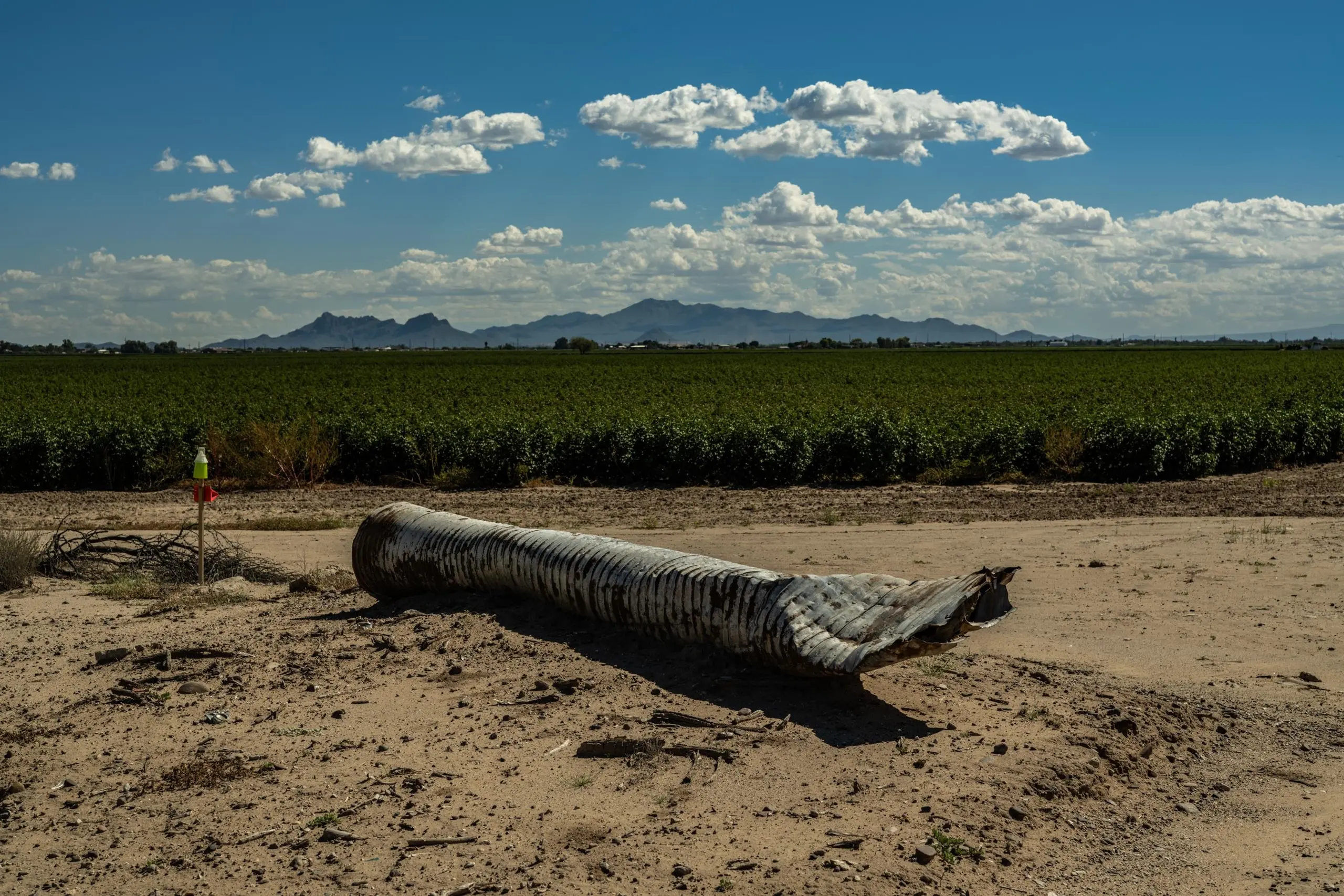 Crushed corrugated pipe in front of a field of crops next to a patch of arid land.